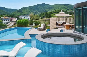 A swimming pool with a hot tub, lounge area, and a view of mountains.