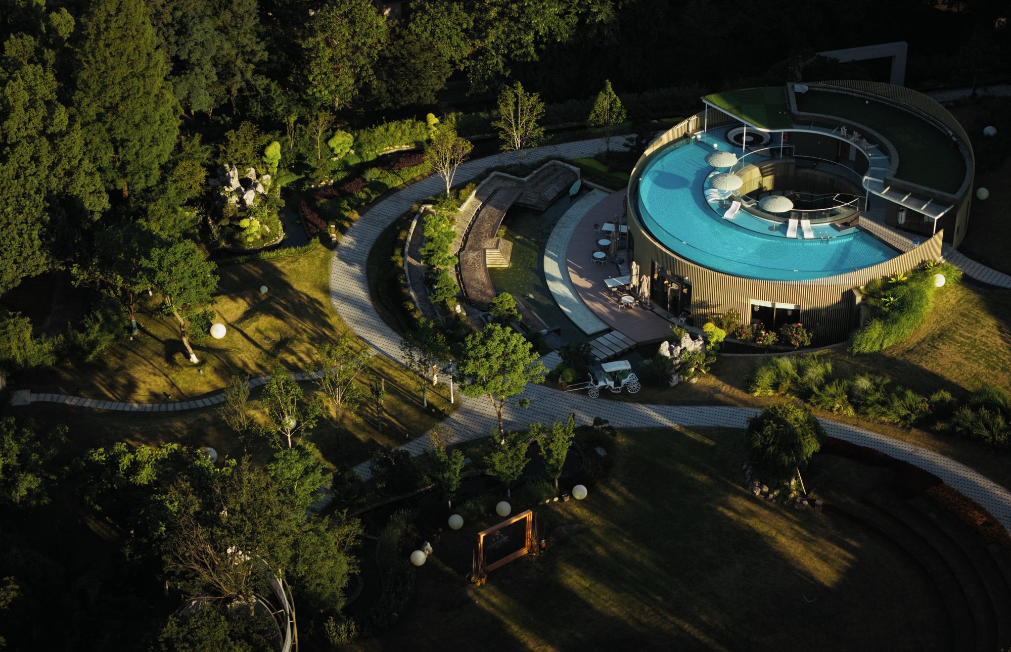 A circular building with a pool, surrounded by a landscaped garden and pathways.