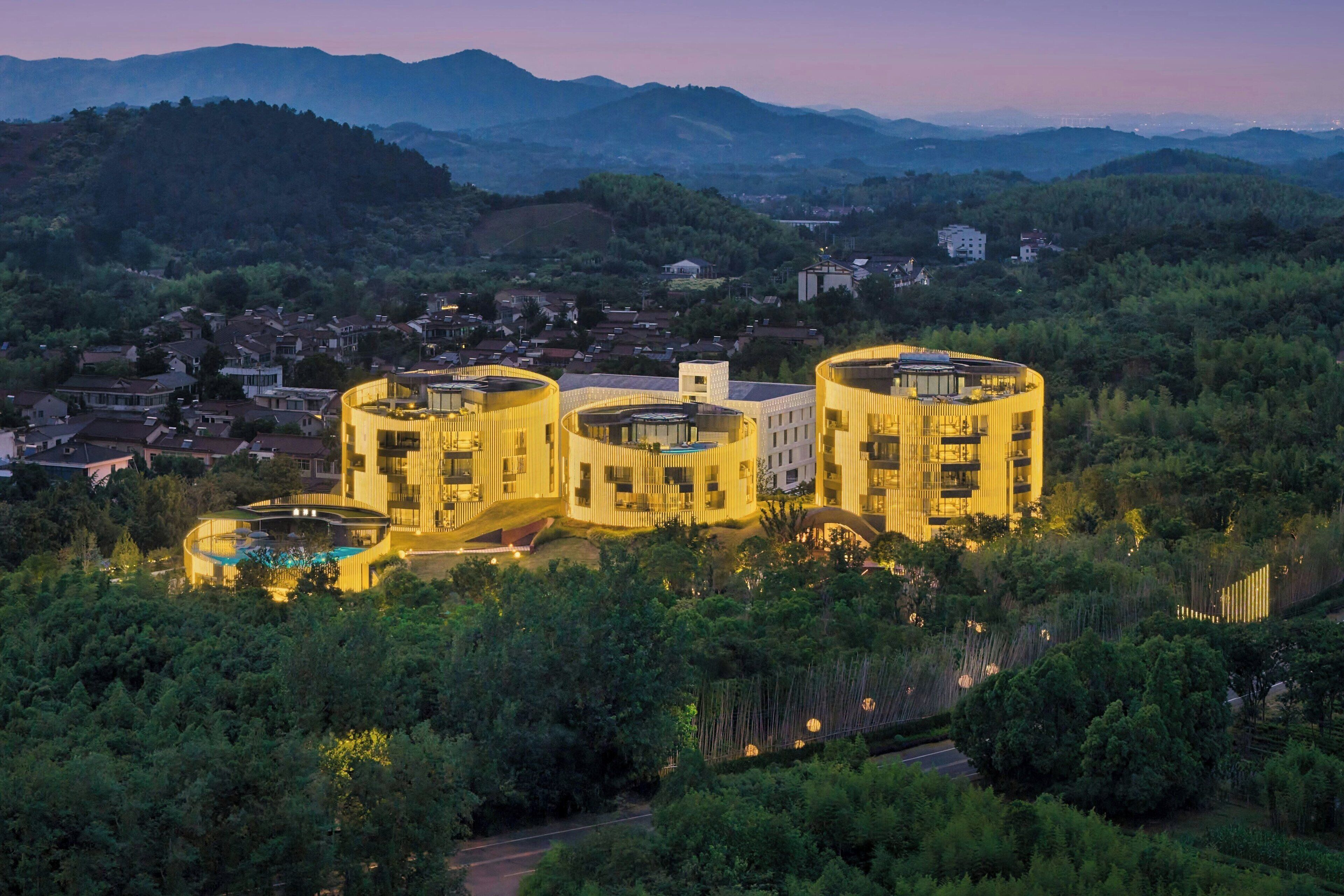 Un edifici modern amb disseny circular, envoltat de vegetació exuberànt i un paisatge amb turons.
