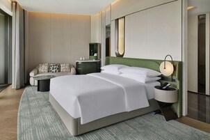 Una habitación de hotel moderna con una cama grande, un sofá, una mesita auxiliar, una mesita de noche y un espejo.