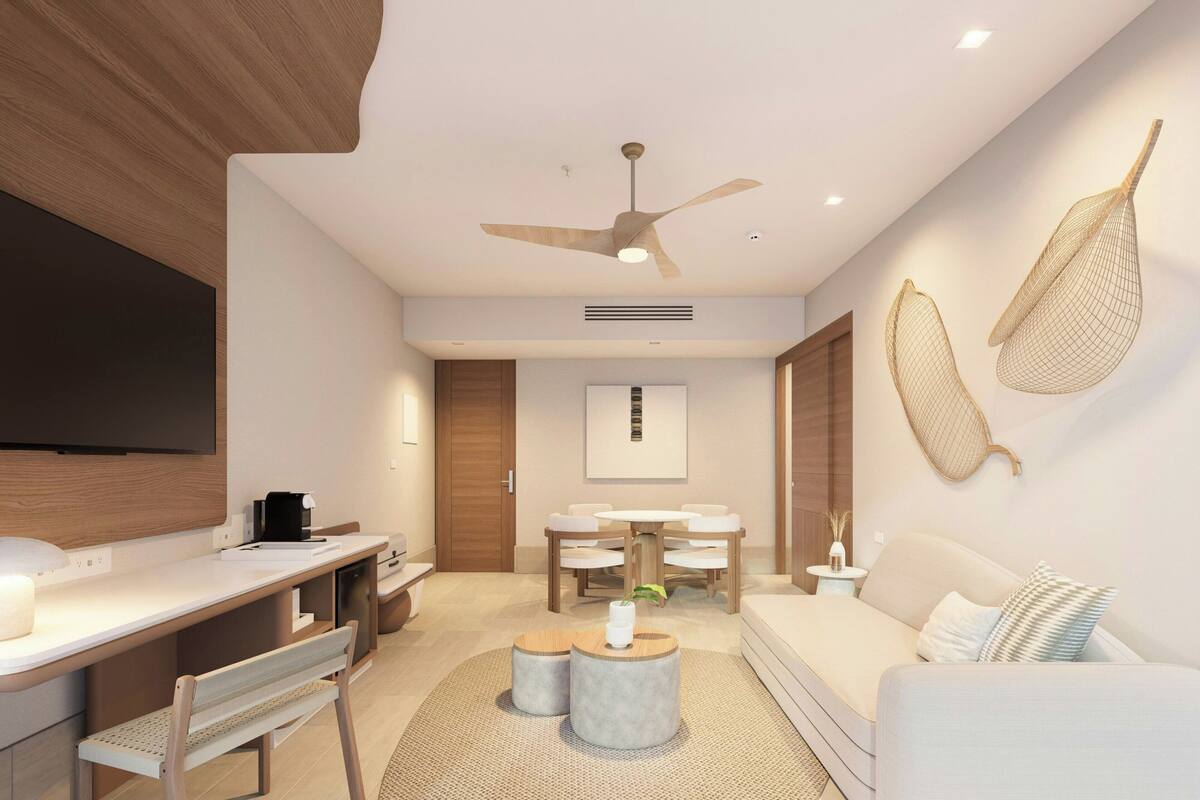 Une chambre d’hôtel moderne équipée d’une télévision à écran plat, d’un bureau avec une chaise, d’un canapé, d’un ventilateur de plafond et d’un coin repas avec une table et des chaises.
