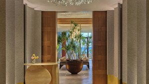 Un couloir avec une grande plante en pot, une table ronde en bois et un coin salon avec des chaises.