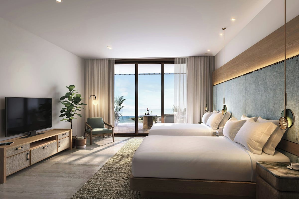 A modern hotel room with a large bed, a TV, a plant, and a view of the ocean.