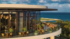 Un bâtiment moderne avec une façade en verre, des places assises en plein air et une vue sur l’océan.