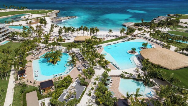 Un complexe hôtelier doté de plusieurs piscines, de palmiers et offrant une vue sur l’océan.