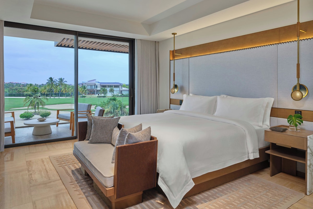 A modern hotel room with a large bed, a seating area, and a view of a golf course.