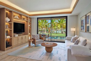 A modern living room with a flat-screen TV, a sofa, a coffee table, and a view of a pool and palm trees.