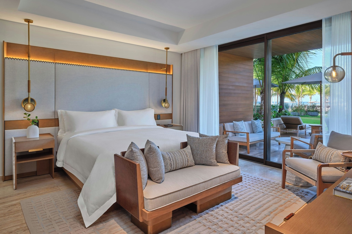 A modern hotel room with a large bed, a sofa, and a view of the outdoors.