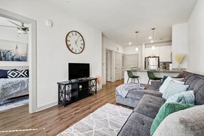 A modern living room with a flat-screen TV, a large clock, and a cityscape view. - Luxury 1BR Near NoDa & Uptown Charlotte (Charlotte)