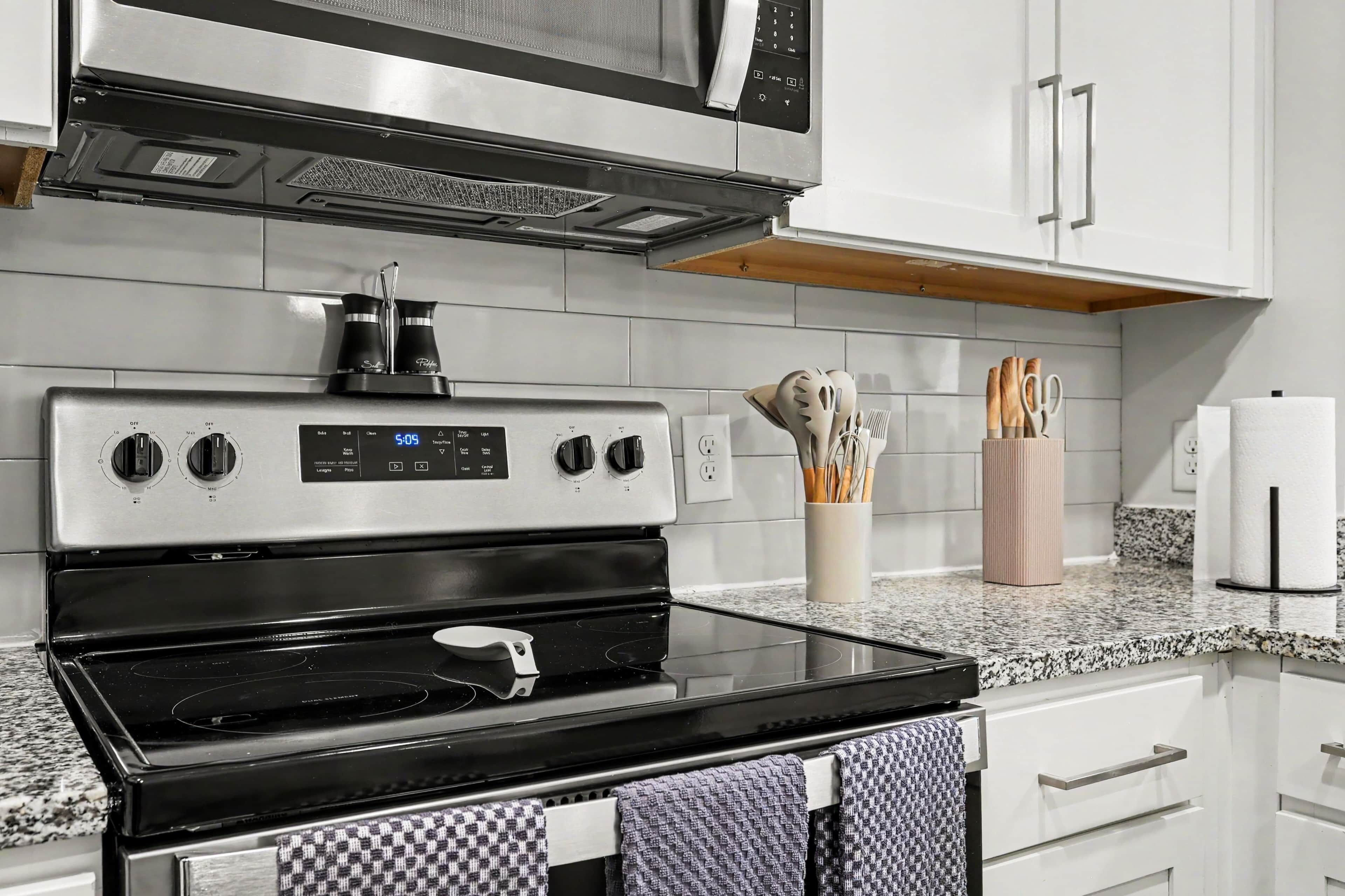A kitchen with a stainless steel stove, microwave, and oven. There are cabinets, a countertop, and a towel rack.