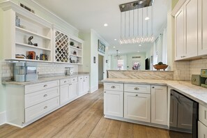 A kitchen with white cabinetry, a marble countertop, and a built-in dishwasher. - Spacious + Luxurious New Orleans Escape • Treat Yourself (New Orleans)