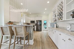 A modern kitchen with white cabinetry, a central island with chairs, a stainless steel refrigerator, and a wine rack. - Spacious + Luxurious New Orleans Escape • Treat Yourself (New Orleans)
