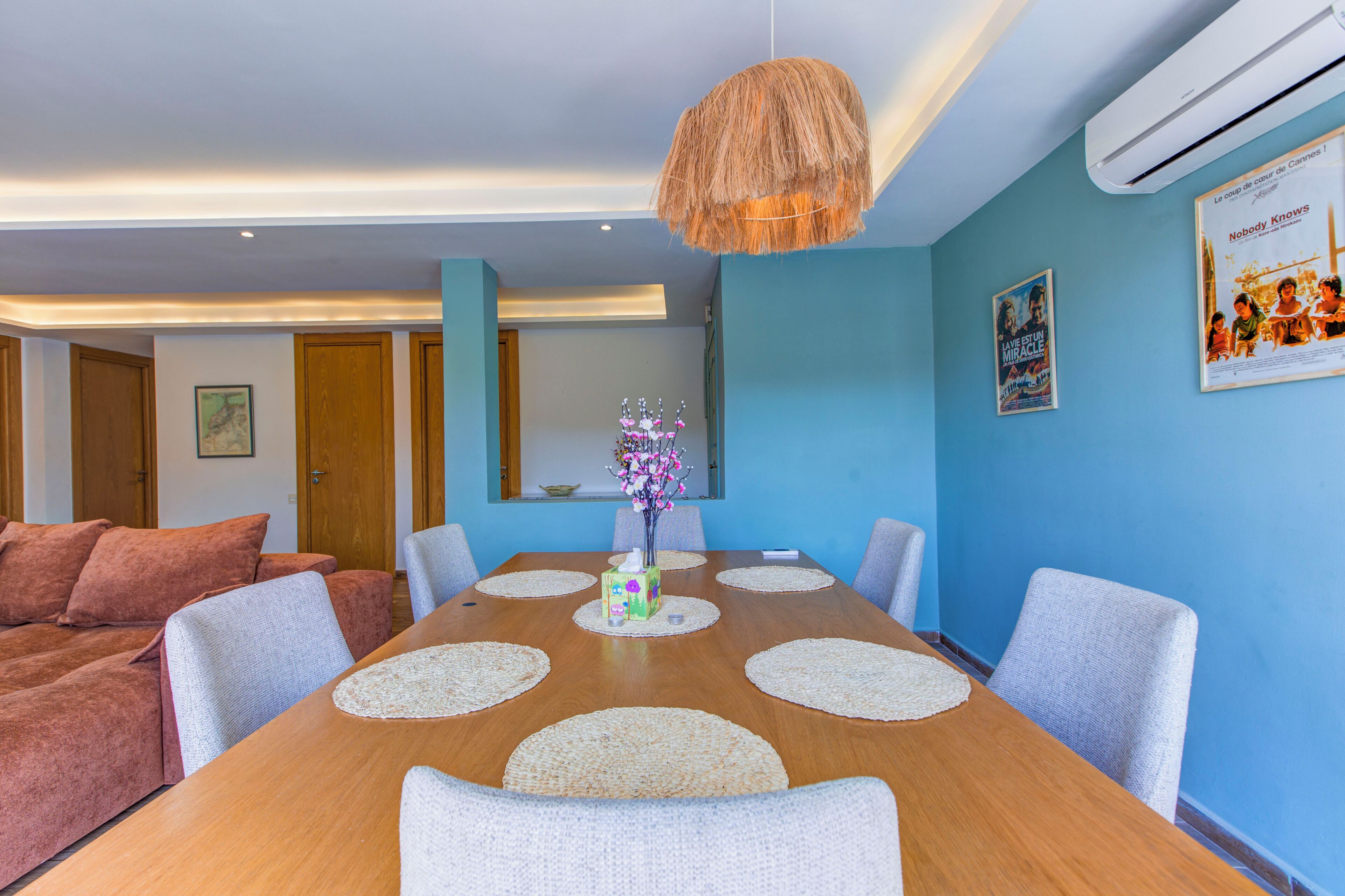 A dining area with a wooden table, white placemats, and a hanging light fixture.