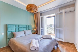 A modern bedroom with a large bed, a hanging light fixture, and a view through an open door. - Mohammed VI | Elegant 3-bedroom apartment with a terrace (Maroc)