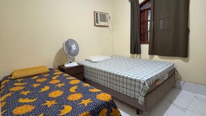 Een slaapkamer met twee bedden, een ventilator, een airconditioning en een raam met gordijnen.