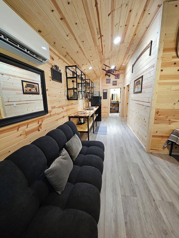 Una habitación acogedora con un sofá negro, paredes de madera y un techo con vigas a la vista.