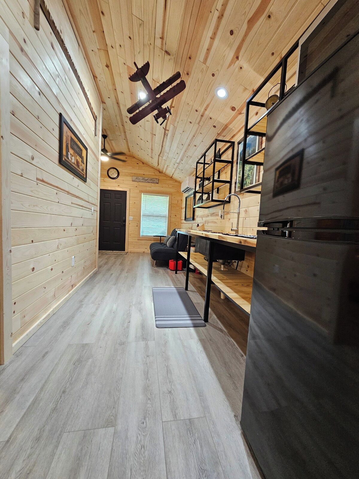 A wooden interior with a ceiling fan, a refrigerator, and a bench.