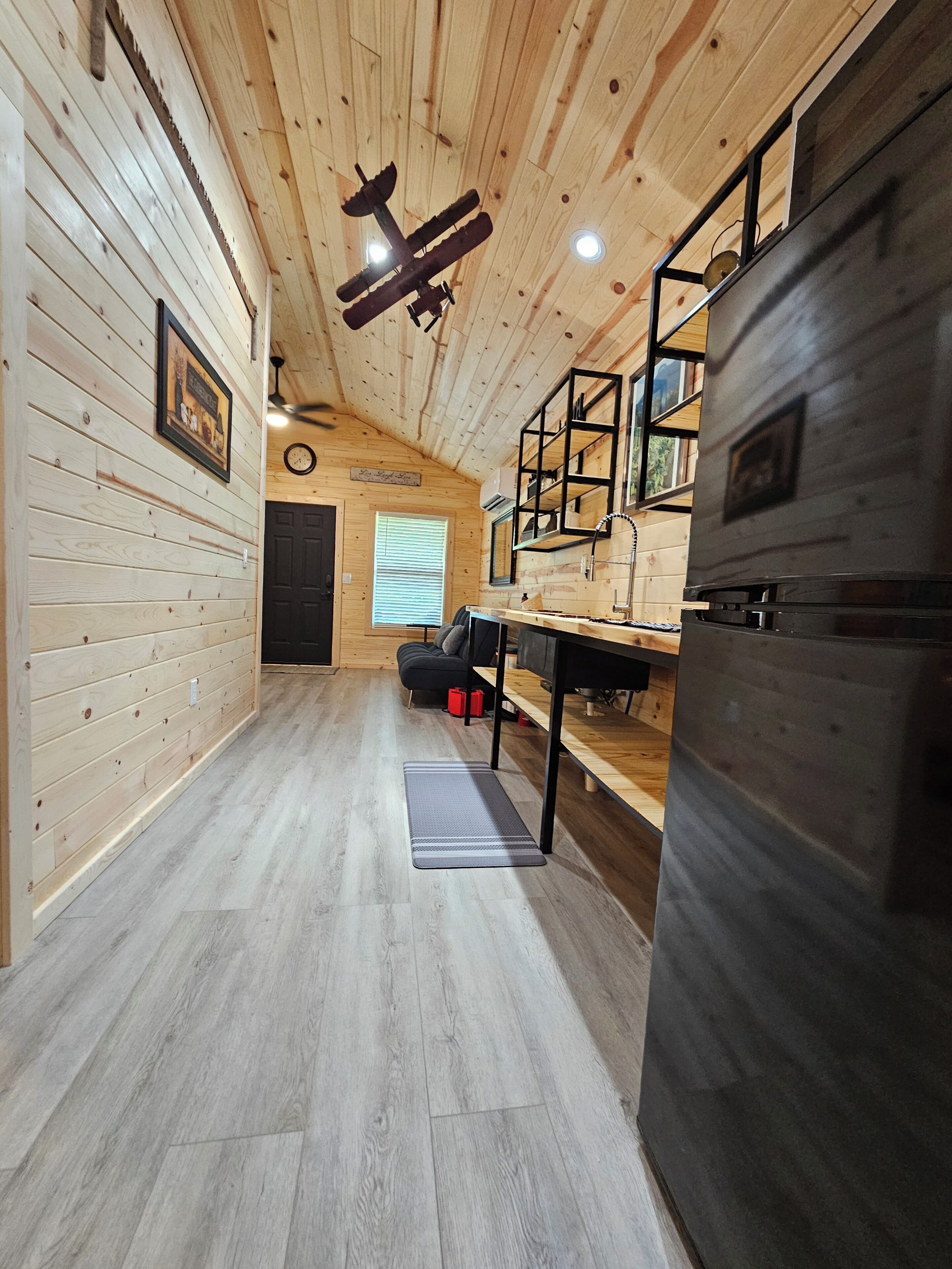 Een houten interieur met plafondventilator, een koelkast, een tafel en een bank.