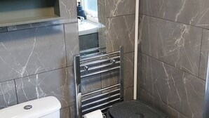 Ein Badezimmer mit Toilette, Mülleimer, Handtuchhalter und Duschbereich.
