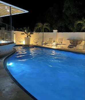 A swimming pool with lounge chairs and umbrellas, surrounded by a white wall and palm trees. - Boutique Sal (Acapulco)