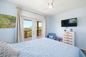Ein Schlafzimmer mit einem Bett, einem Fernseher, einem Sessel, einer Kommode und einer Balkontür.