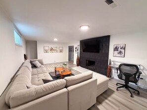 Una sala de estar moderna con un sofá modular, una mesa de centro de vidrio, una chimenea y un televisor montado en la pared.