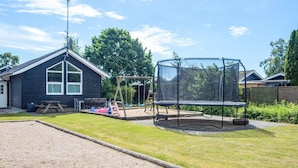 A residential backyard with a trampoline, wooden play structures, and a house with a dark exterior and white trim. - 5 Star Holiday Home in Hadsund (Hadsund)
