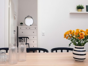 Un coin repas avec une table en bois, des chaises, un vase de fleurs et une commode avec un miroir.