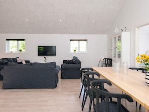 Ein modernes Wohnzimmer mit einer Sofagarnitur, einem Fernseher und einem Essbereich mit Stühlen und einem Tisch.