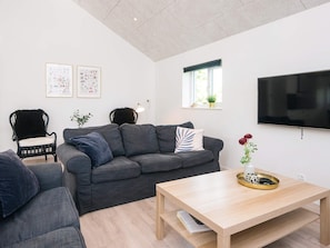 Un salon moderne avec un canapé gris, une table basse en bois, un fauteuil noir et un téléviseur fixé au mur.