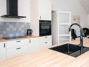 Eine moderne Küche mit einer schwarzen Dunstabzugshaube, weißen Schränken, einem eingebauten Ofen und einem schwarzen Spülbecken mit einem modernen Wasserhahn.