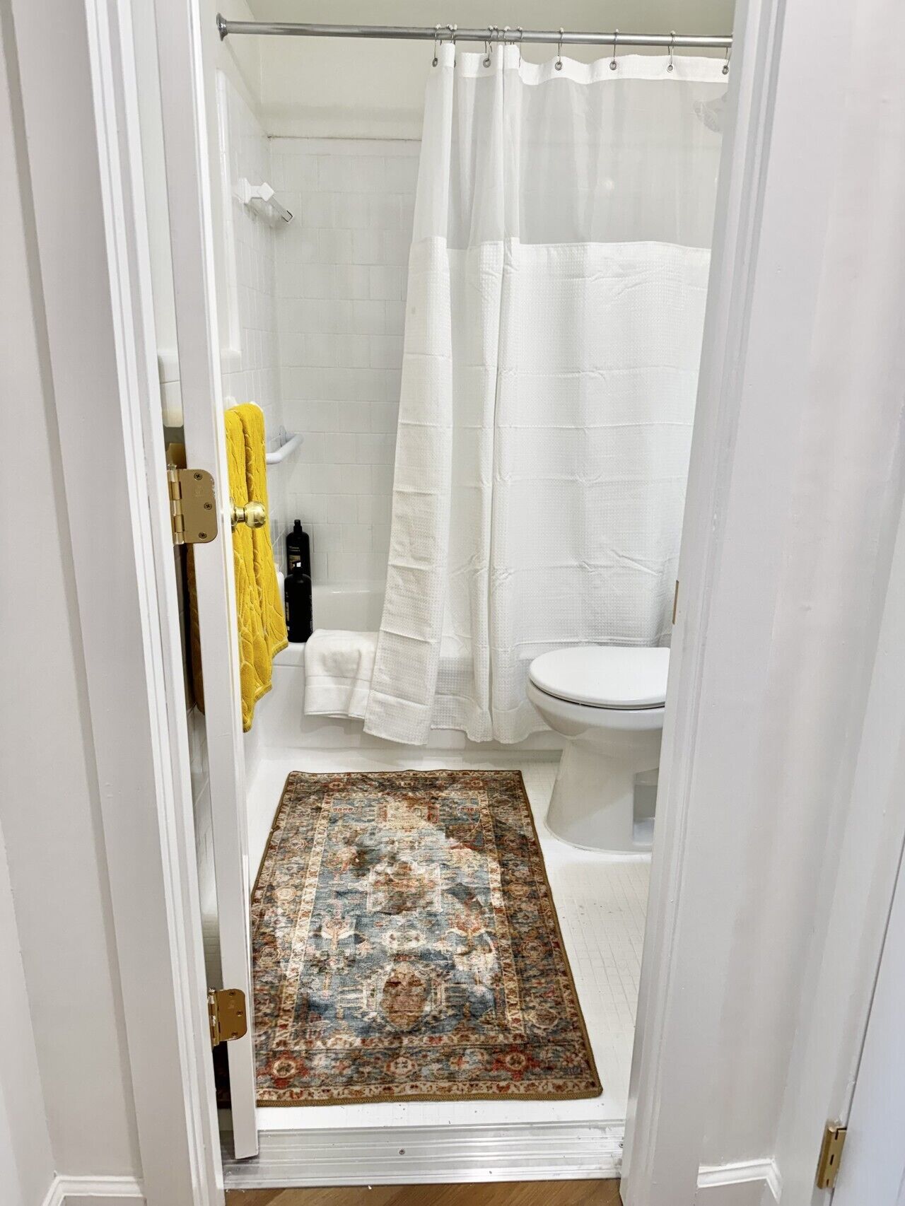 A bathroom with a shower curtain, a toilet, and a patterned rug.