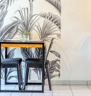 A dining area with a table, two chairs, and a wall with a leaf pattern. - XAVIER – F2 cosy avec balcon à Rouen (Rouen)