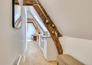 A modern interior with exposed wooden beams, a kitchen area, and a hallway leading to a bedroom. - JACKY - Joli 2 pièces avec vue sur l'Eglise Saint Maclou (Rouen)