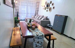 Ein Wohnzimmer mit einer Couch, einem Couchtisch, einem Esstisch mit Bänken, einem Schrank und Wanddekorationen.