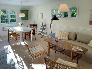 A well-lit room with a dining table, chairs, a sofa, and a floor lamp. - Holiday home with orangery and private garden (Vejby)