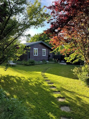 A house with a well-maintained lawn, a stone pathway leading to the entrance, and a variety of trees in the background. - Holiday home with orangery and private garden (Vejby)