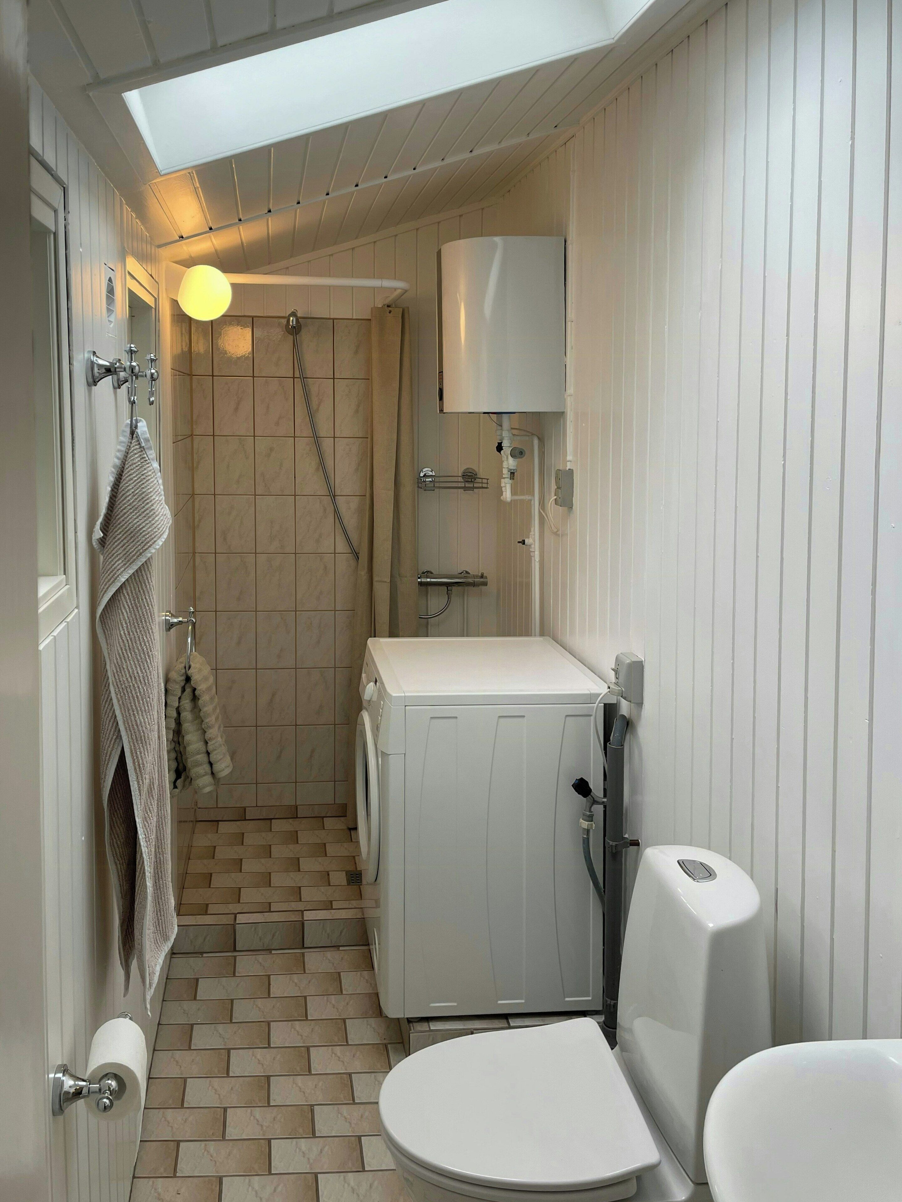 Een kleine badkamer met een douche, toilet en een wasmachine.