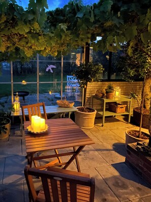 An outdoor patio with a wooden table and chairs, potted plants, and a view of a park. - Holiday home with orangery and private garden (Vejby)