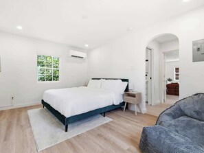 A bedroom with a bed, a nightstand, a window, and a door leading to another room. - Modern 1BR on Main St in Bishop Arts (Dallas)