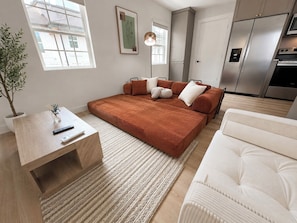 Ein modernes Schlafzimmer mit einem großen Bett, einem Nachttisch, einem weißen Sofa und einer Küchenzeile mit Kühlschrank und Backofen.