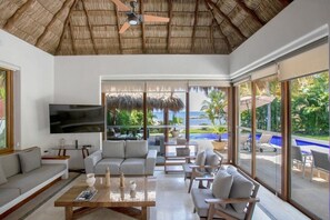 A spacious living area with a large TV, comfortable seating, and a view of a pool and ocean. - Beachfront Villa with Pool & Ocean Views (Cruz de Huanacaxtle)
