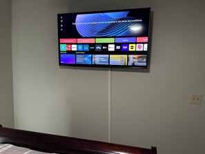 Televisor de pantalla plana montado en una pared que muestra una interfaz de usuario con varios iconos de aplicaciones y opciones.