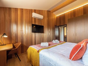 Ein Hotelzimmer mit Holzwandverkleidung, einem Flachbildfernseher, einem Schreibtisch mit Lampe, einem Bett mit Kissen und einer Klimaanlage.