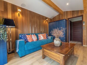 Ein Zimmer mit einem blauen Sofa, Holzwänden, einem Holztisch und einer Tür mit digitalem Schloss.