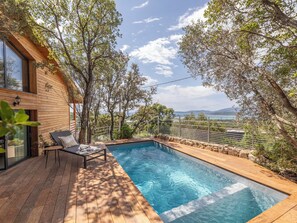 Eine Holzterrasse mit Pool, Liegestuhl und Blick aufs Meer.