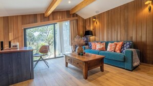Un soggiorno moderno con soffitto in legno, un divano blu con cuscini decorati, un tavolino in legno e un'ampia finestra con tende.