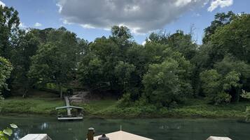 Une terrasse en bois mène à un espace abrité situé au bord d’une rivière, où un bateau est amarré à proximité.