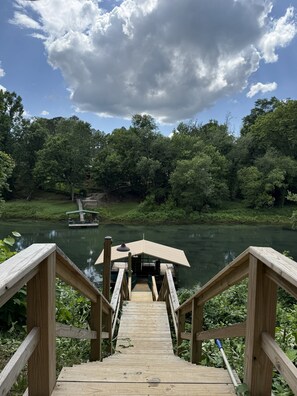A wooden deck leading to a covered area by a river with a boat docked nearby. - The Great Troutdoors, Heber Springs, AR (Heber Springs)