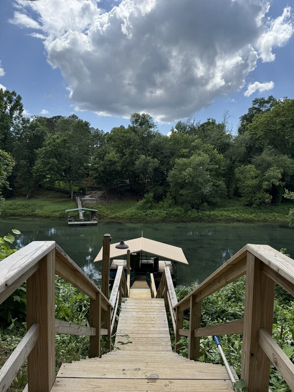 A wooden deck leading to a covered area by a river with a boat docked nearby.